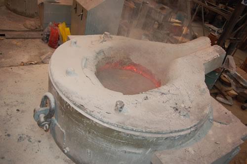 a foundry induction furnace containing molten steel with a layer of insulating kiesselguhr powder reducing heat loss from the surface.